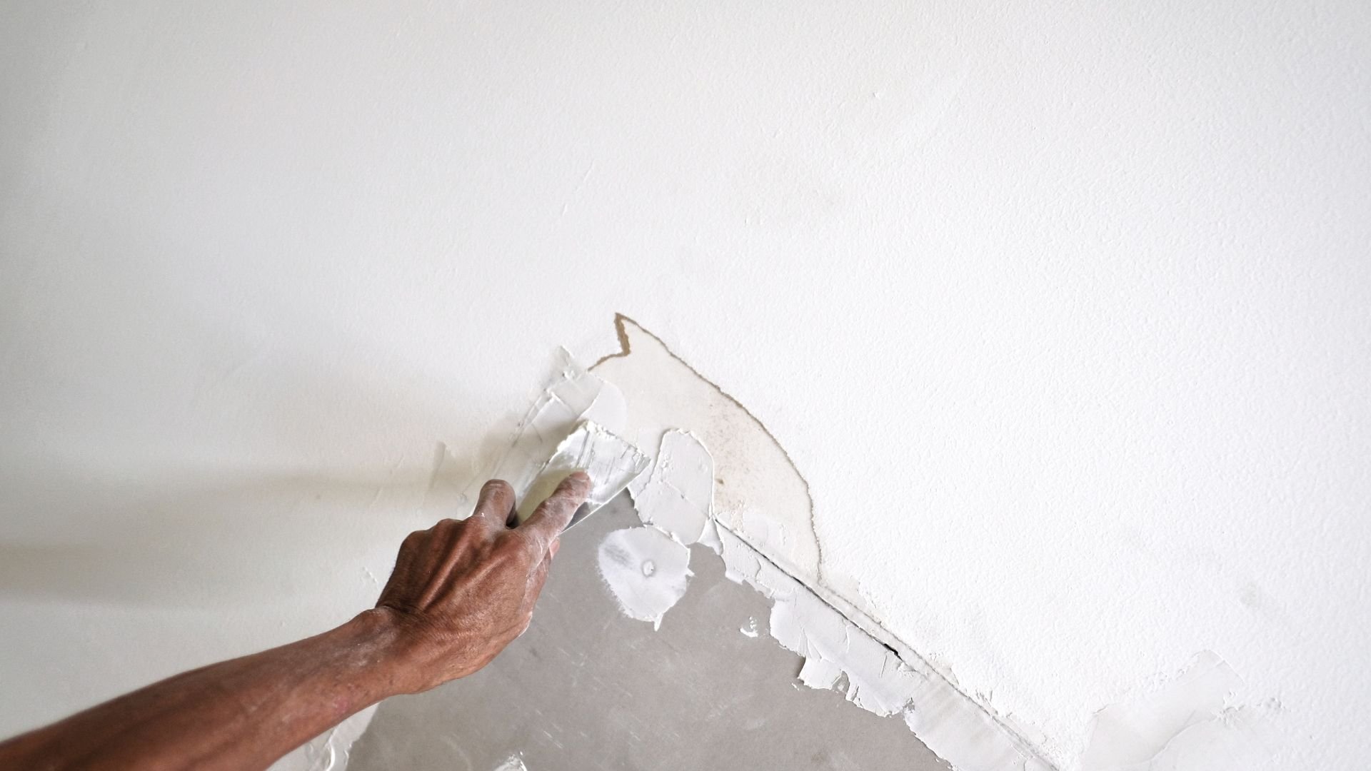 Hand scraping paint off white wall during home renovation project