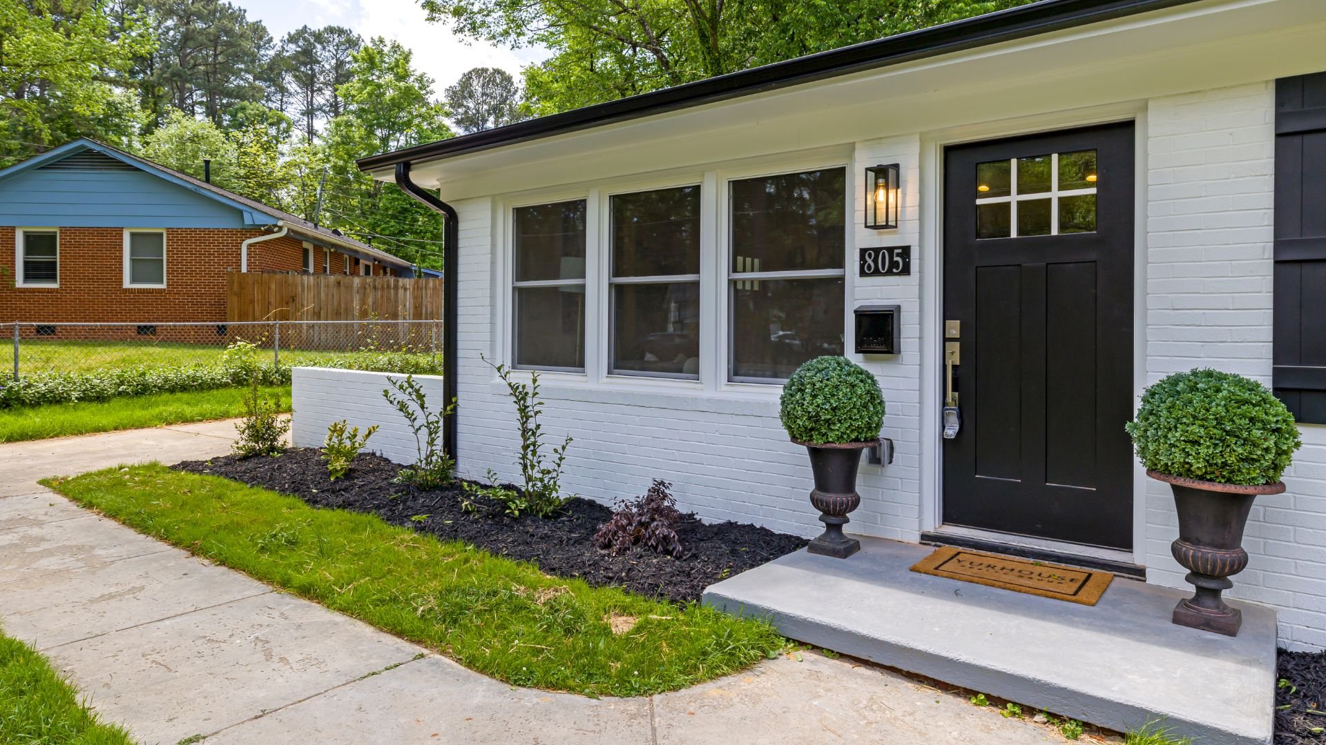 White brick house with black door, topiary, and welcome mat