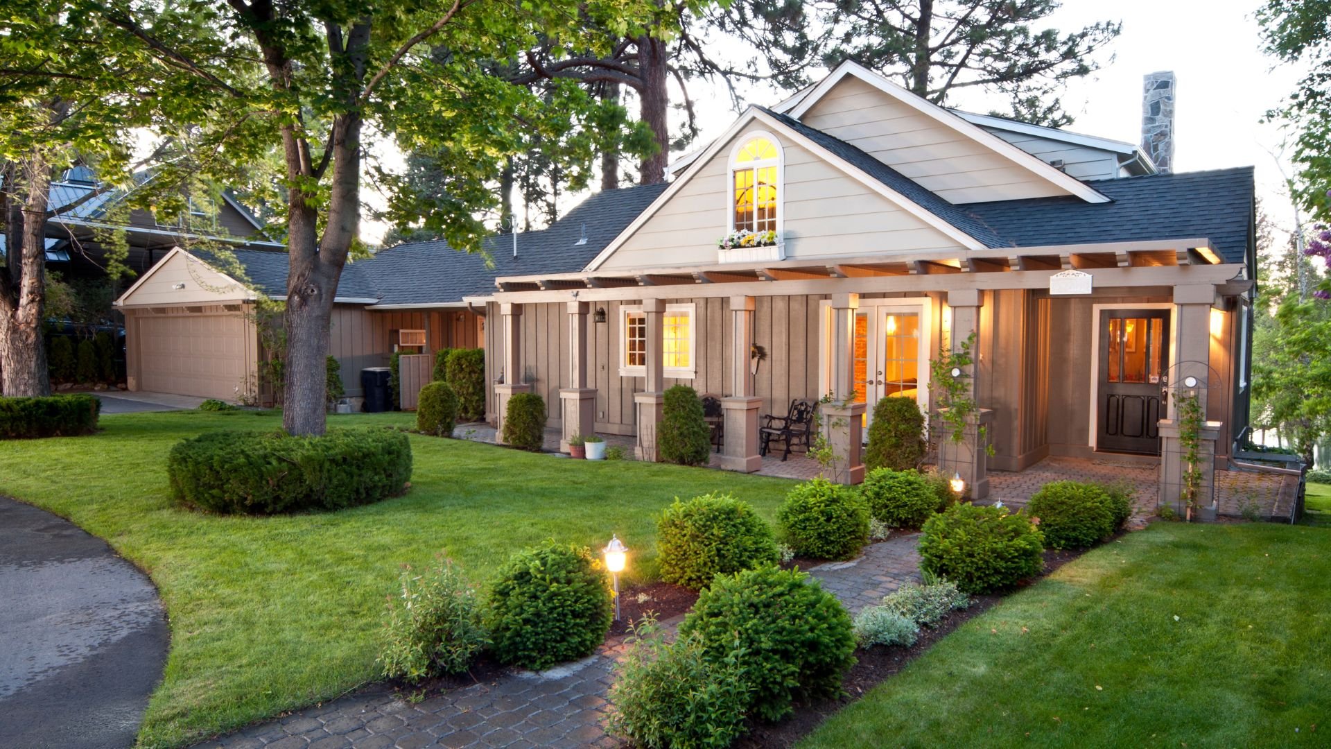 Well-manicured suburban home with warm lighting and landscaped garden at dusk