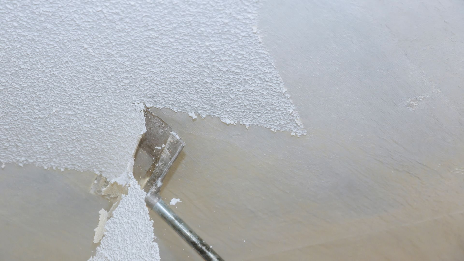 Scraping paint or wallpaper with a metal putty knife from a textured surface