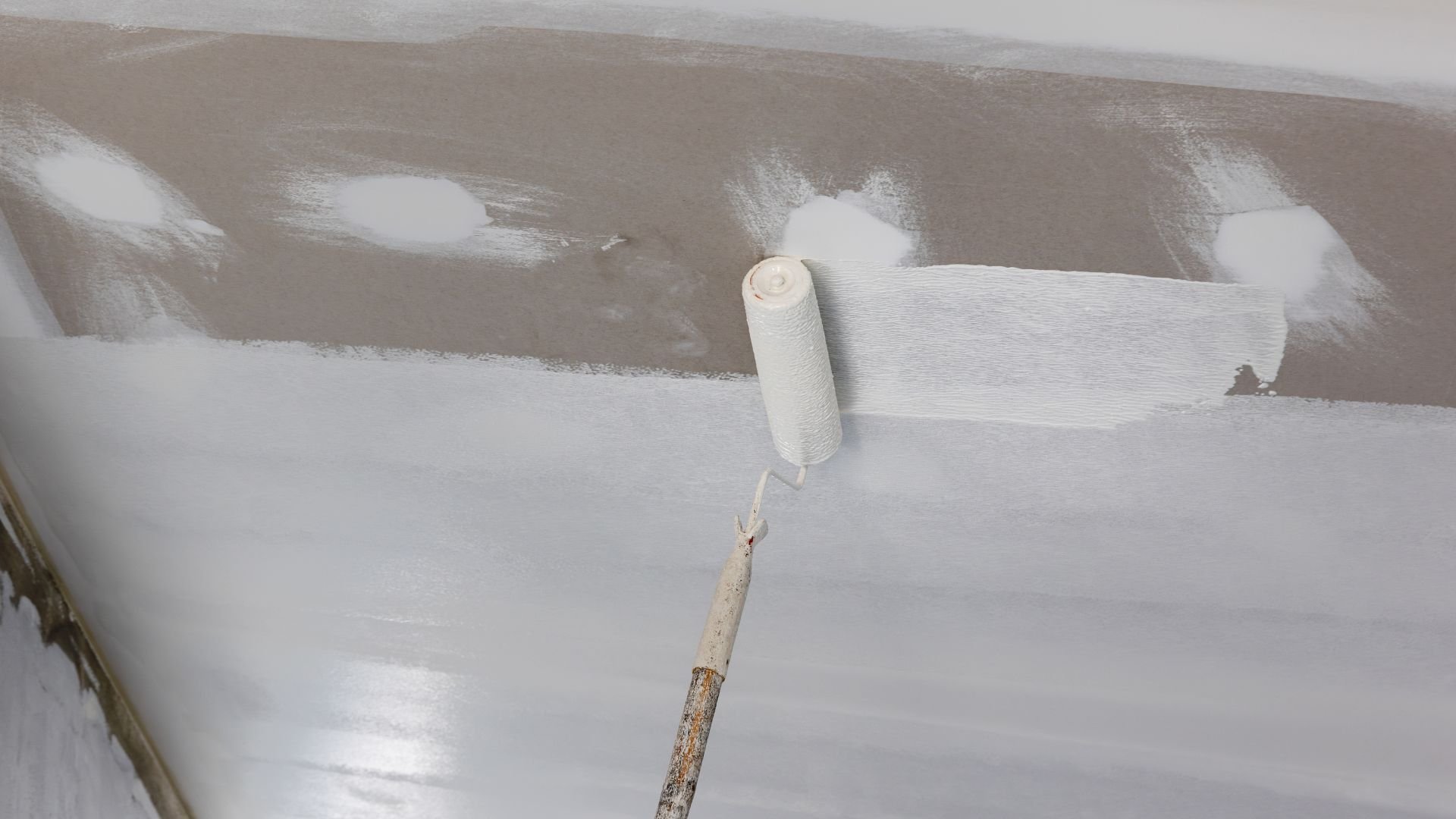 Paint roller applying white paint on wall during home renovation project