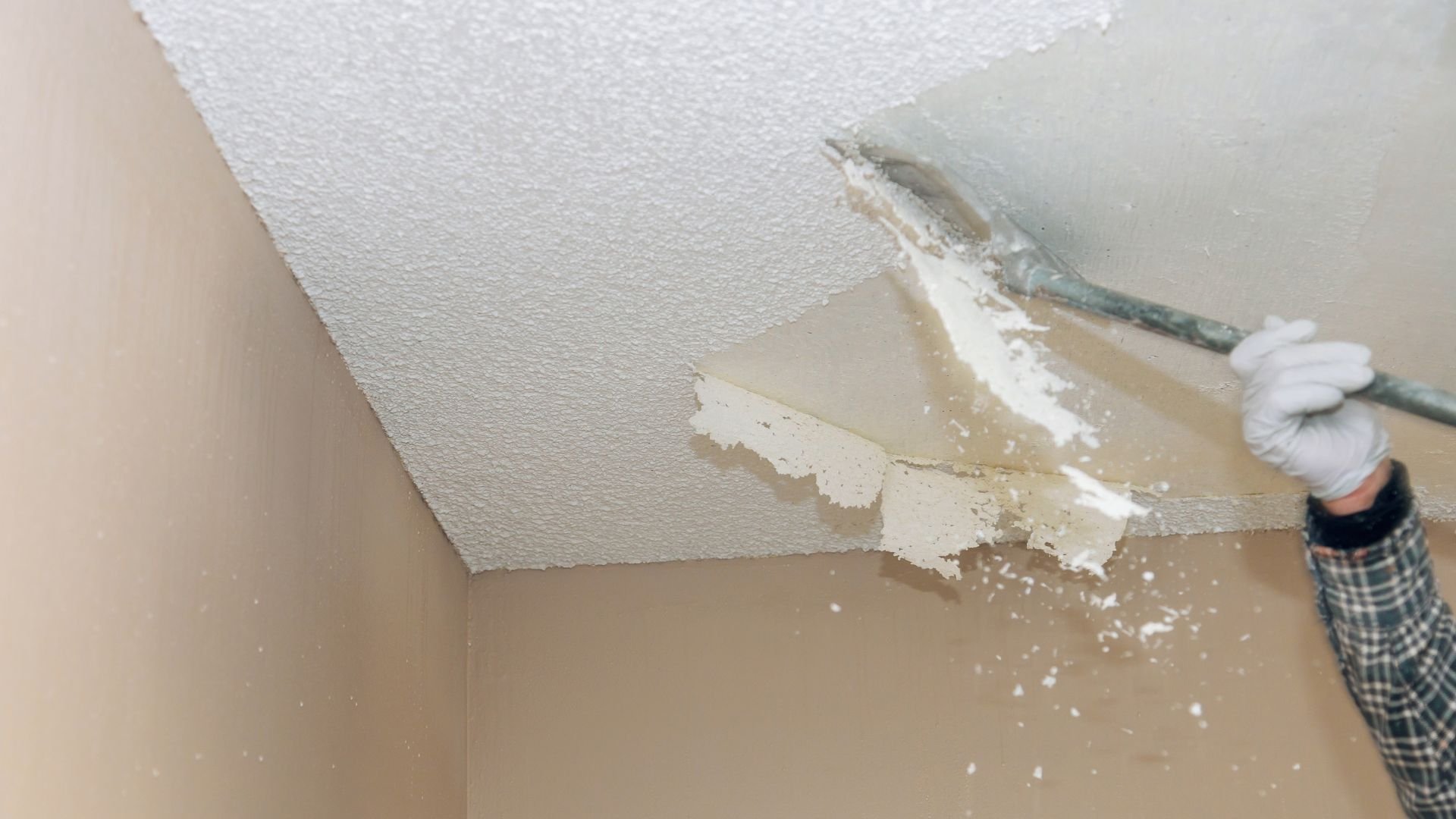 Removing textured ceiling with scraper, white plaster falling down